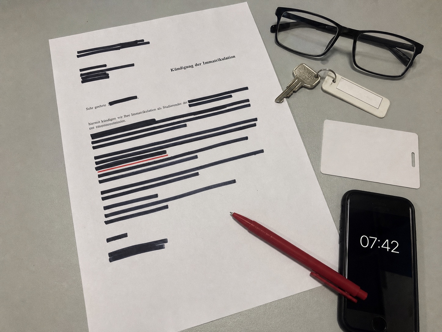 Geschwärztes Schreiben, Schlüssel, Brille und Telefon mit der Uhrzeit 07:42